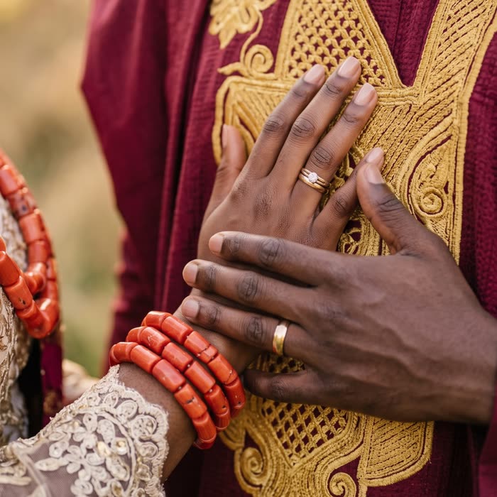 Their hands with coral bead bracelets on his embroidered agbada